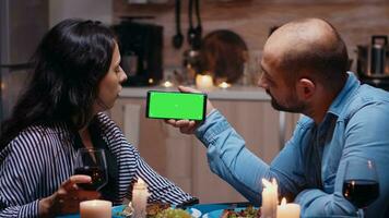 marié Jeune couple en portant maquette téléphone à dîner. content à la recherche à vert écran modèle chrominance clé isolé intelligent téléphone afficher en utilisant technologie l'Internet séance à le table dans cuisine. photo