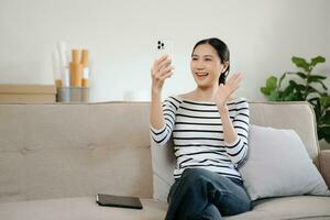 Jeune asiatique femme en utilisant téléphone intelligent et tablette tandis que assise sur canapé à Accueil photo