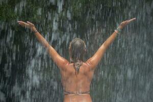 magnifique Jeune femme se détend en dessous de une cascade. sexy fille dans une bikini posant près une cascade dans le tropiques. photo