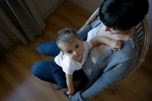 une Jeune femme détient sa peu fils dans sa bras tandis que séance dans une confortable fauteuil photo