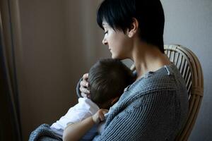 une Jeune femme détient sa peu fils dans sa bras tandis que séance dans une confortable fauteuil photo