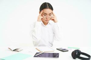 lieu de travail et entreprise. portrait de fatigué femme dans bureau, entreprise employé est assis à bureau avec épuisé affronter, touche sa diriger, a mal de tête, blanc Contexte photo