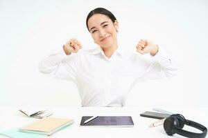 lieu de travail et affaires concept. souriant magnifique asiatique femme, Bureau ouvrier est assis dans bureau, s'étire sa mains avec heureux visage après terminé travail, blanc Contexte photo