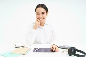 réussi Jeune asiatique femme dans écouteurs, est assis dans bureau, lieu de travail, souriant et à la recherche professionnel, blanc Contexte photo