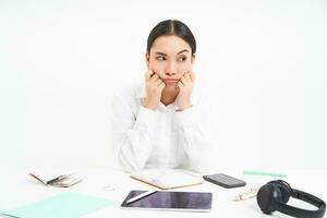 ennuyé Jeune asiatique femme d'affaires, est assis dans sa Bureau à lieu de travail, regards de côté dérangé et fatigué, des stands plus de blanc Contexte photo