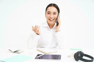 image de Bureau employé, asiatique femme dans Bureau pourparlers sur mobile téléphone, discute travail sur téléphone portable, blanc Contexte photo