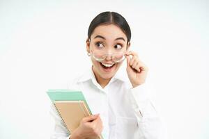 portrait de entreprise femme, asiatique femme dans lunettes, détient carnet et regards surpris, étonné par qch, des stands plus de blanc Contexte photo