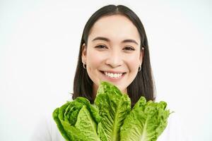 proche en haut portrait de content coréen femme, spectacles sa visage avec laitue, en mangeant chou, aime légumes, se sent en bonne santé et sous tension, blanc Contexte photo