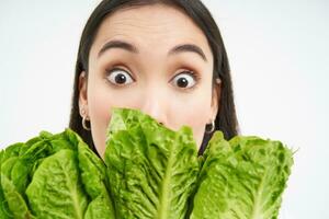 portrait de mignonne Jeune femme spectacles sa visage avec chou, aime légumes, mange en bonne santé nutritif régime nourriture, détient laitue, blanc Contexte photo