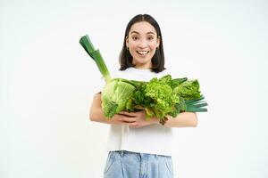 portrait de content Jeune femme sur vert régime, aime en mangeant biologique nourriture, en portant Frais des légumes de jardin, laitue, chou, blanc studio Contexte photo