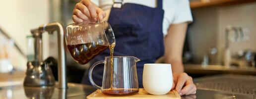 proche en haut de verre pot et une tasse permanent sur café comptoir, barista verser filtre café et en train de préparer commande photo