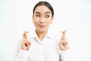 proche en haut portrait de optimiste femme d'affaires, traverser les doigts pour bien chance, attend pour quelque chose, fait du souhait, sourit et anticipe, blanc studio Contexte photo