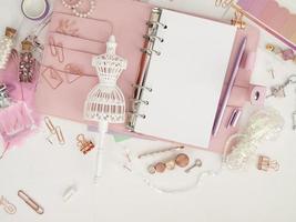 vue de dessus d'un agenda rose avec une jolie papeterie. planificateur glamour rose avec une figurine mannequin blanche. planificateur avec pages ouvertes sur fond blanc et avec de beaux accessoires stylos, boutons, épingles. photo