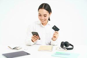 entreprise et entreprise. asiatique femme dans bureau, détient téléphone intelligent et crédit carte, payant en ligne, réglage en haut direct débit en ligne, blanc Contexte photo