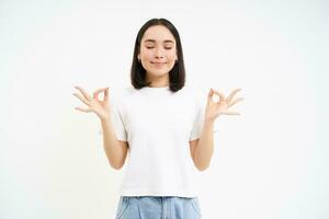 paisible souriant asiatique femme, permanent calme et détendu, détient mains dans Zen, méditation pose, isolé plus de blanc Contexte photo