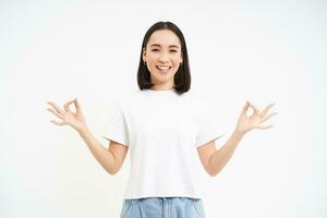 paisible souriant asiatique femme, permanent calme et détendu, détient mains dans Zen, méditation pose, isolé plus de blanc Contexte photo