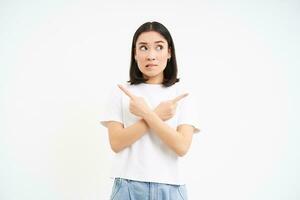 en pensant asiatique fille fait du sa décision, points de côté, deux façons, choisir, des stands isolé sur blanc Contexte photo