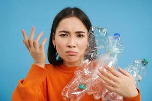 femme avec en colère affronter, en portant bouteilles, recyclage Plastique déchets, se plaindre, permanent plus de bleu Contexte photo