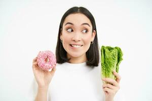 en bonne santé mode de vie concept. content souriant asiatique femme, montrant un vitré Donut et chou, donnant choix, blanc Contexte photo