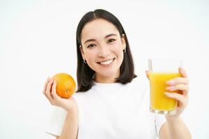 proche en haut portrait de brunette fille, 25 années, en portant Frais verre de jus et Orange fruit, souriant, mange en bonne santé nourriture, blanc Contexte photo