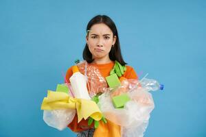 dérangé fille a à recycler, détient Plastique bouteilles et litière, à la recherche dérangé et en colère, bleu Contexte photo