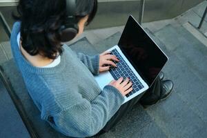 proche en haut portrait de fille, étudiant travaux sur portable et écoute la musique dans écouteurs. Vide ordinateur écran et mains dactylographie sur clavier photo