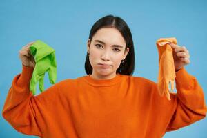 image de fille avec dérangé affronter, montrant deux sale nettoyage gants, a trouvé ordures, à la recherche déçu, bleu Contexte photo