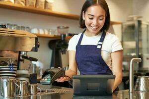 souriant asiatique barista fille En traitement commande, entrer commande dans pos Terminal, travail à compteur dans café magasin photo