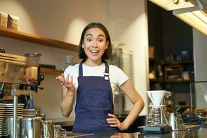 portrait de fille barista dans tablier, regards surpris, points avec main et regarde étonné à caméra, travaux derrière compteur et brasseries café photo