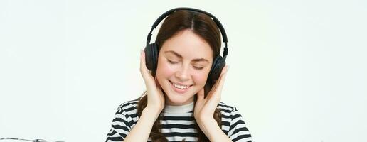 portrait de femme, souriant, portant sans fil écouteurs, écoute musique, en train d'étudier dans écouteurs, permanent isolé plus de blanc Contexte photo