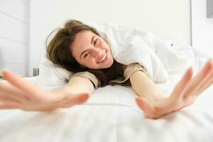 magnifique fille en riant et souriant, élongation dans Hôtel lit, profiter somnolent matin, bien sieste photo