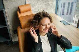 image de femme dans conférence chambre, femme d'affaires travail dans sa Bureau dans de face de le fenêtre, répondre une téléphone appel et en riant photo