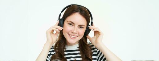 proche en haut portrait de mignonne Jeune femme, souriant, en mettant sur écouteurs, écoute à la musique dans écouteurs, en essayant sur Nouveau casque, blanc Contexte photo