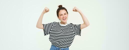 femme Puissance et féminisme. Jeune fille sentiment habilité et fort, fléchissement sa biceps, montrant muscles sur bras, permanent plus de blanc Contexte photo