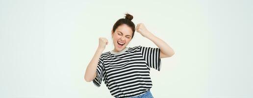 image de excité Jeune fille applaudissement, élevage mains en haut, cris de excitation et bonheur, gagnant, célébrer la victoire, permanent plus de blanc Contexte photo