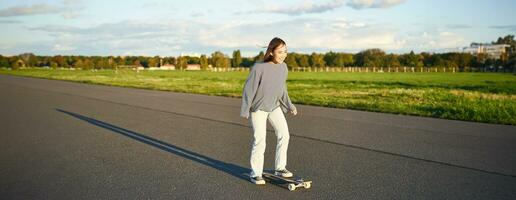 loisirs et mode de vie. Jeune femme équitation planche à roulette. patineur fille profiter croisière sur longboard sur ensoleillé journée en plein air photo