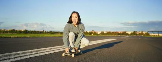 portrait de insouciant, content asiatique fille patinage, équitation planche à roulette et en riant, profiter ensoleillé journée photo