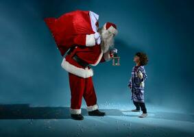 Père Noël claus est donnant une présent pour Noël à une peu garçon photo