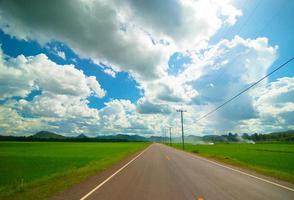 route goudronnée à travers le champ vert et nuages sur ciel bleu en été photo