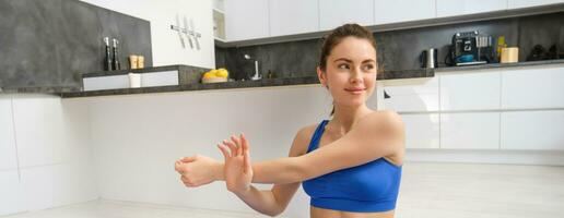 magnifique et en forme femme Est-ce que faire des exercices à maison, s'étire sa bras, Est-ce que réchauffer avant formation des exercices, porte soutien-gorge de sport, est assis sur caoutchouc yoga tapis photo