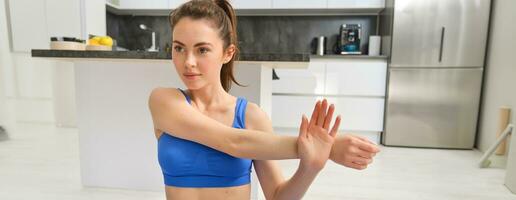 proche en haut coup de femme Faire faire des exercices de maison, réchauffer élongation mains, Est-ce que aptitude des exercices dans bleu soutien-gorge de sport et souriant photo