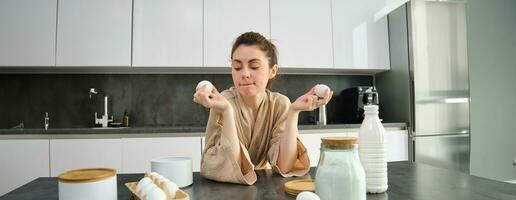 attrayant Jeune de bonne humeur fille cuisson à le cuisine, fabrication pâte, en portant recette livre, ayant des idées photo