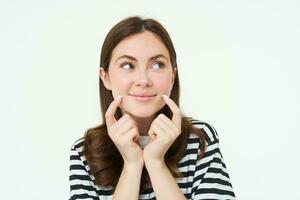 beauté et femmes concept. Jeune souriant femme, montrant sa mignonne fossettes sur visage et à la recherche content, positif émotion, magnifique visage sans pour autant les imperfections, permanent plus de blanc Contexte photo