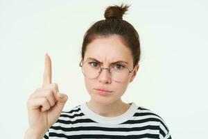 portrait de Jeune femme, tuteur dans lunettes, montrer du doigt doigt en haut et renfrogné, montrant qch important, permanent plus de blanc Contexte photo