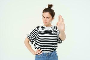 image de magnifique femme avec sérieux affronter, montrant Arrêtez signe, étend un paume et fronce les sourcils, des stands plus de blanc Contexte photo