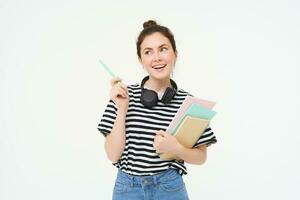 portrait de Jeune femme, étudiant avec des cahiers et écouteurs sur sa cou, posant pour Université publicité, blanc Contexte photo