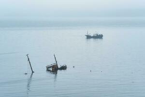 pêche navire et creux Naufrage à mer contre le Contexte de une loin brumeux côte photo