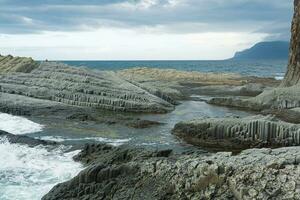 rocheux rivage formé par de colonne basalte contre le toile de fond de une orageux mer, côtier paysage de le kuril îles photo