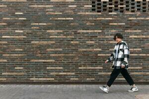 Jeune homme des promenades vers le bas le rue dans de face de une brique mur photo