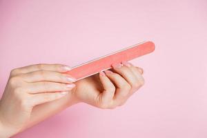 femme fait une manucure à la maison. mains avec une lime à ongles sur fond rose. photo